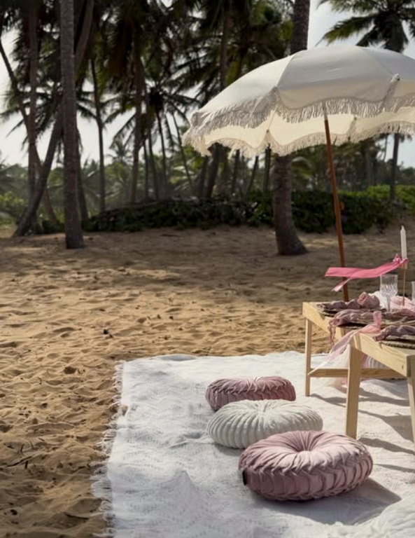 Beach picnic with a fringed umbrella and blush cushions on the sand in Punta Cana.